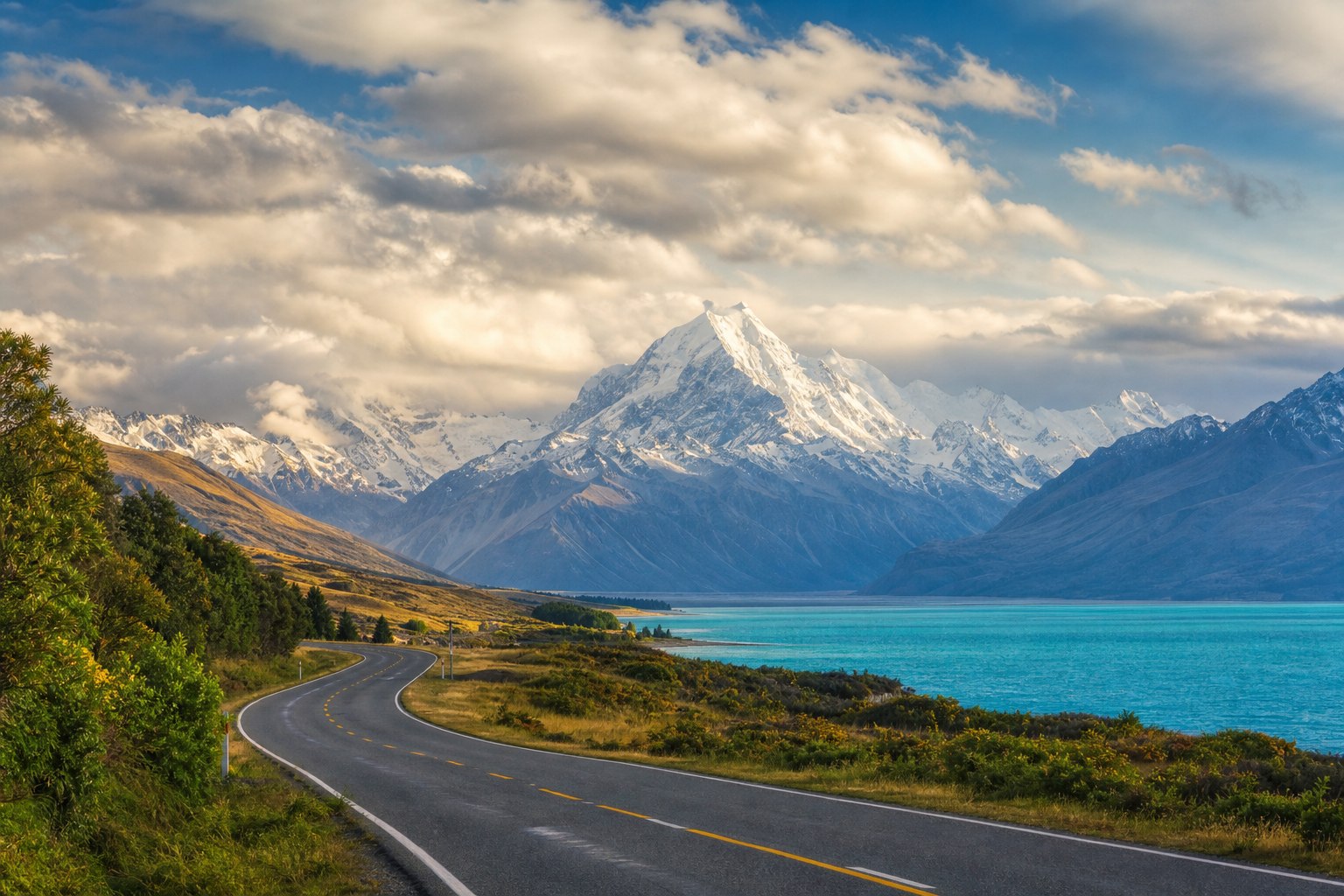Empty highway winding through the New Zealand South Island with snow-capped mountains and a turquoise lake